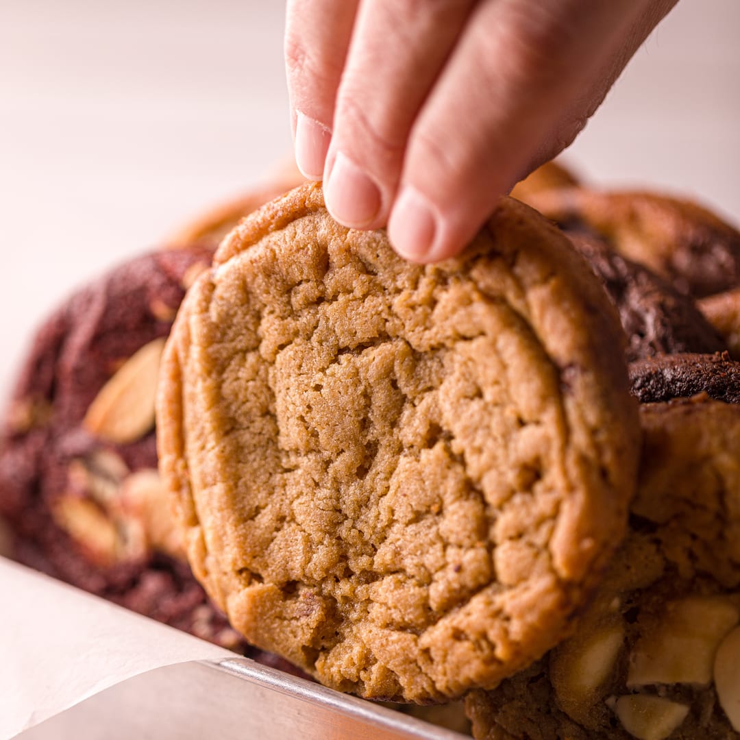 Mão pegando um cookie Monkey da bandeja de sortidos