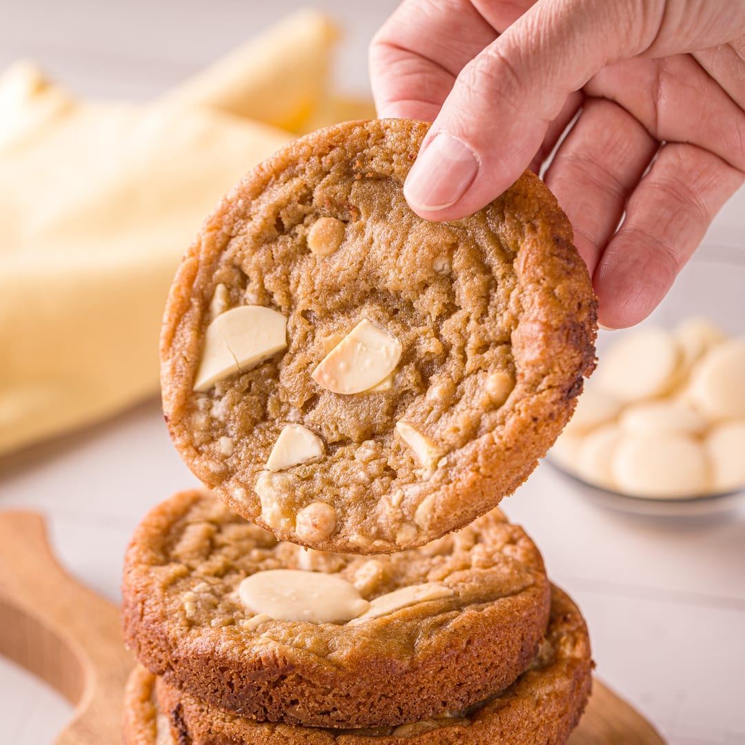 Mão segurando um cookie de chocolate branco sobre a pilha