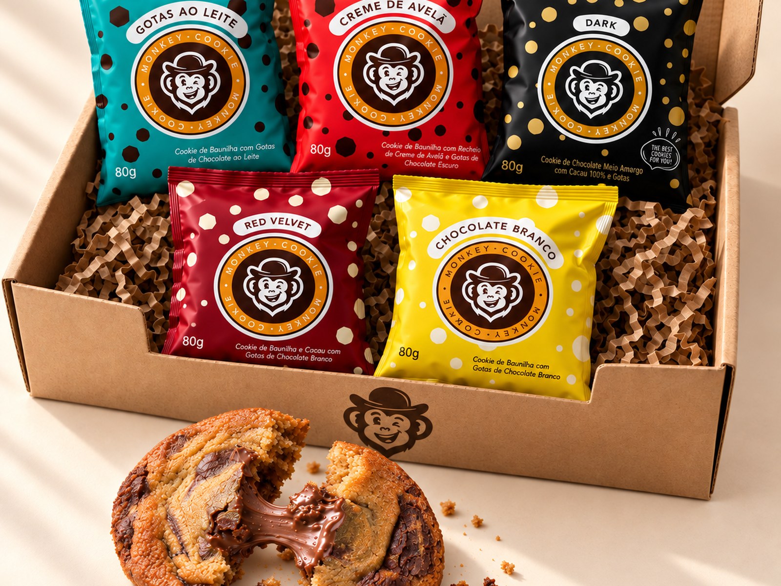 Caixa do Kit 5 Cookies aberta com as cinco embalagens Monkey Cookie e um cookie de creme de avelã partido na frente